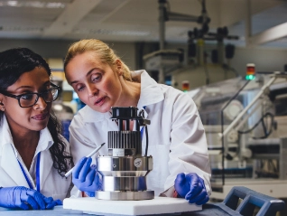 Two female lab workers in white coats and gloves